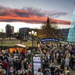 A evening view of the Denver Christkindlmarket with wooden booths and a lighted Christmas tree