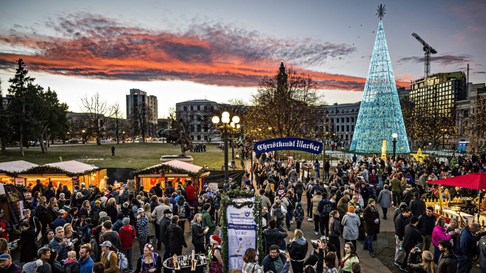 A evening view of the Denver Christkindlmarket with wooden booths and a lighted Christmas tree