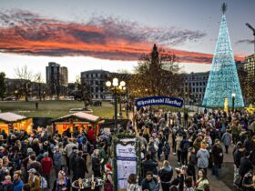 A evening view of the Denver Christkindlmarket with wooden booths and a lighted Christmas tree