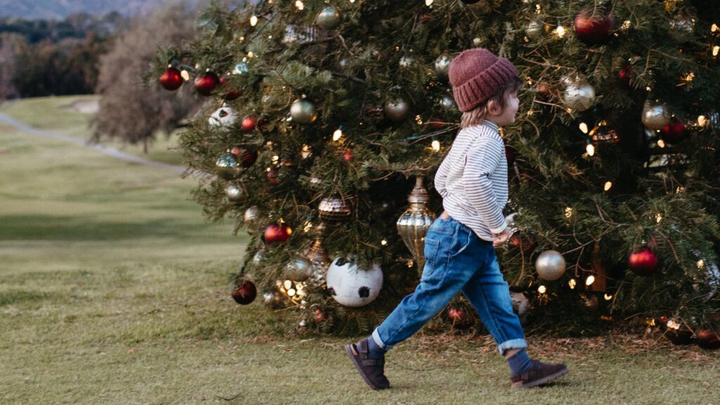 A little kid in a hat running in front of a decorated Christmas tree at Ojai Valley Inn