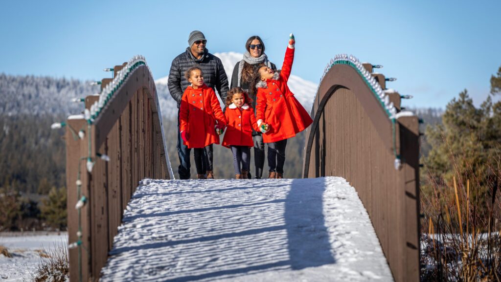 A family with three little girls in red coats walking over a snowy bridge at Sunriver Resort