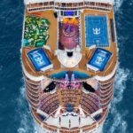 Top deck of cruise ships sailing in ocean, with a sports court, slide, surf simulators, and other features