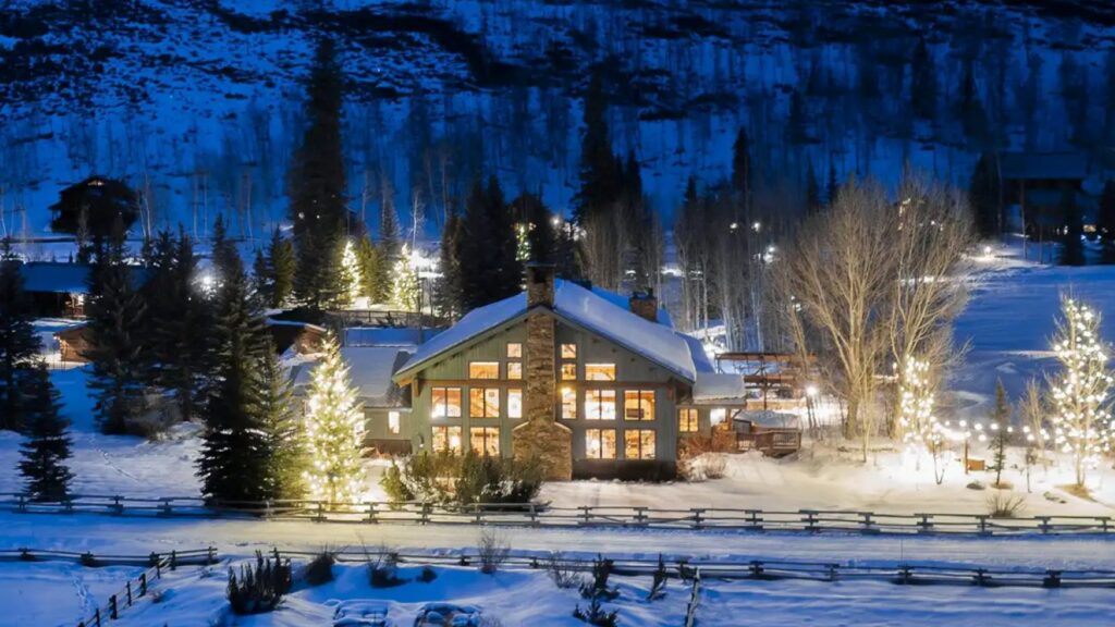 A nighttime view of Vista Verde Ranch with snow and Christmas lights 