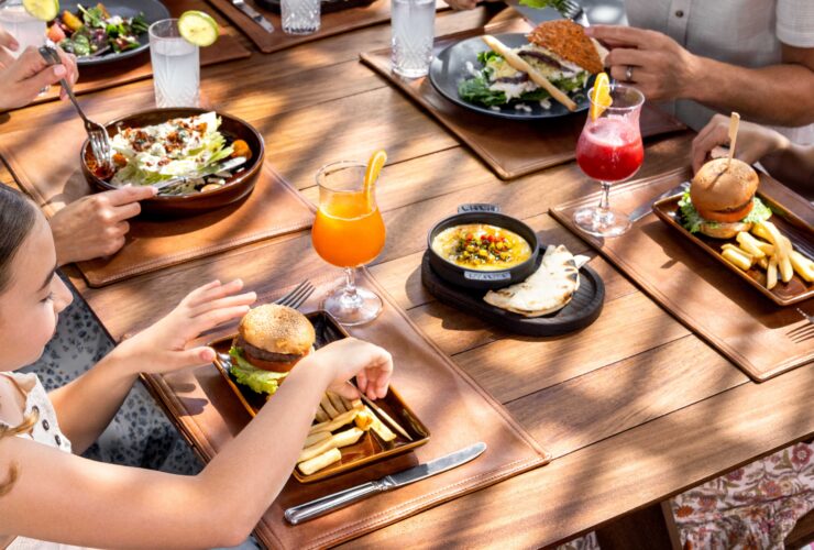 A girl eating a burger at a restaurant with adult family members at Hilton Cancun, an All-Inclusive Resort
