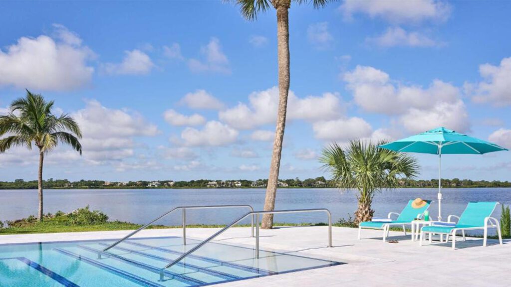 Swimming pool with two lounge chairs under an umbrella, and river in the background