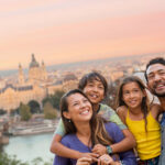 Family hugging each other on top of hill with historic city in the background during sunset