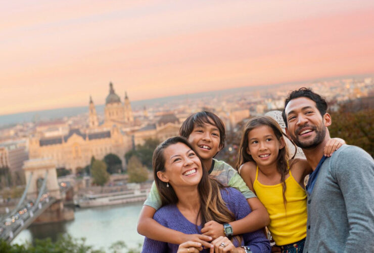 Family hugging each other on top of hill with historic city in the background during sunset