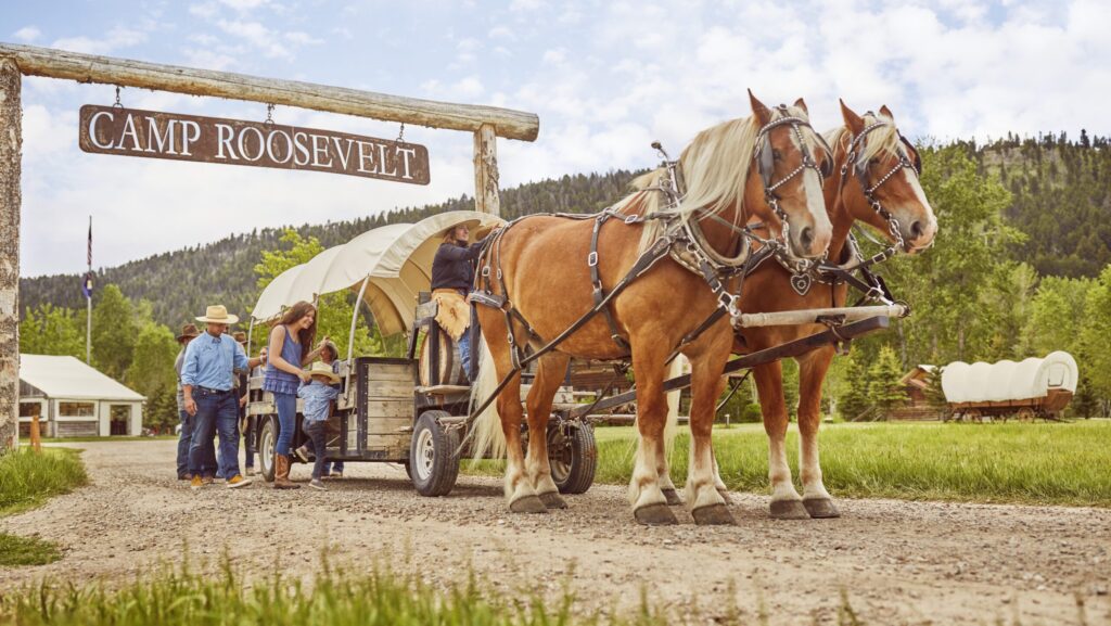 A woman helping a little boy climb into a covered wagon pulled by two horses at The Ranch at Rock Creek