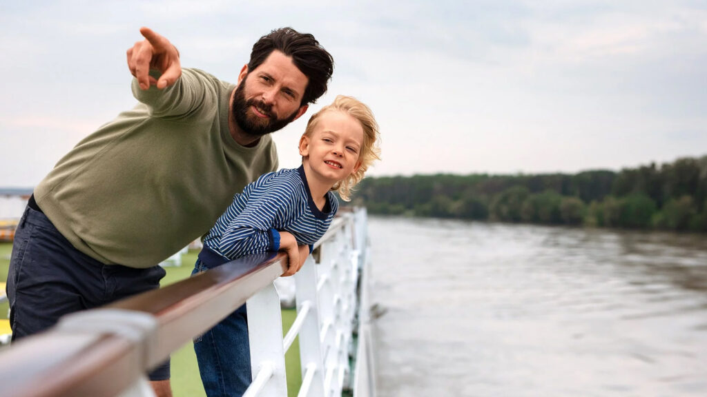 Father and son looking over river cruise ship deck railing