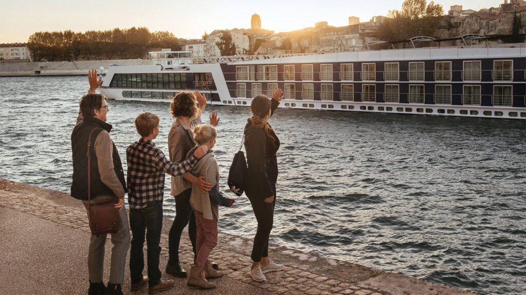 Family facing out toward river and waving at river cruise ship sailing by