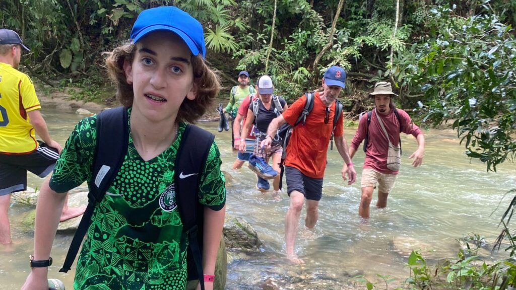 teen crossing a river with a hiking group on the trek to Ciudad Perdida in Colombia