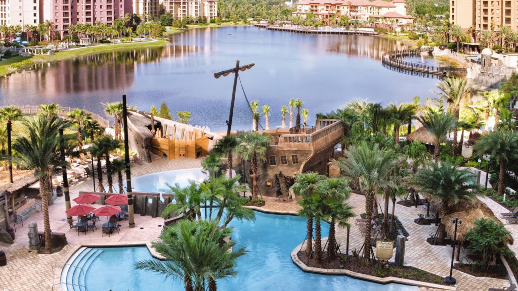 Swimming pool with pirate ship structure next to a lake with buildings in the background