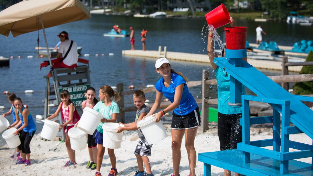 Kids and counselors playing a game with buckets of water on the beach at The Pines at Woodloch