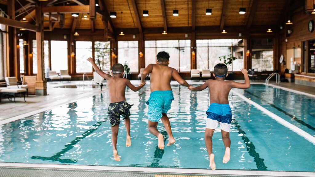 Three kids holding hands and jumping in to an indoor pool