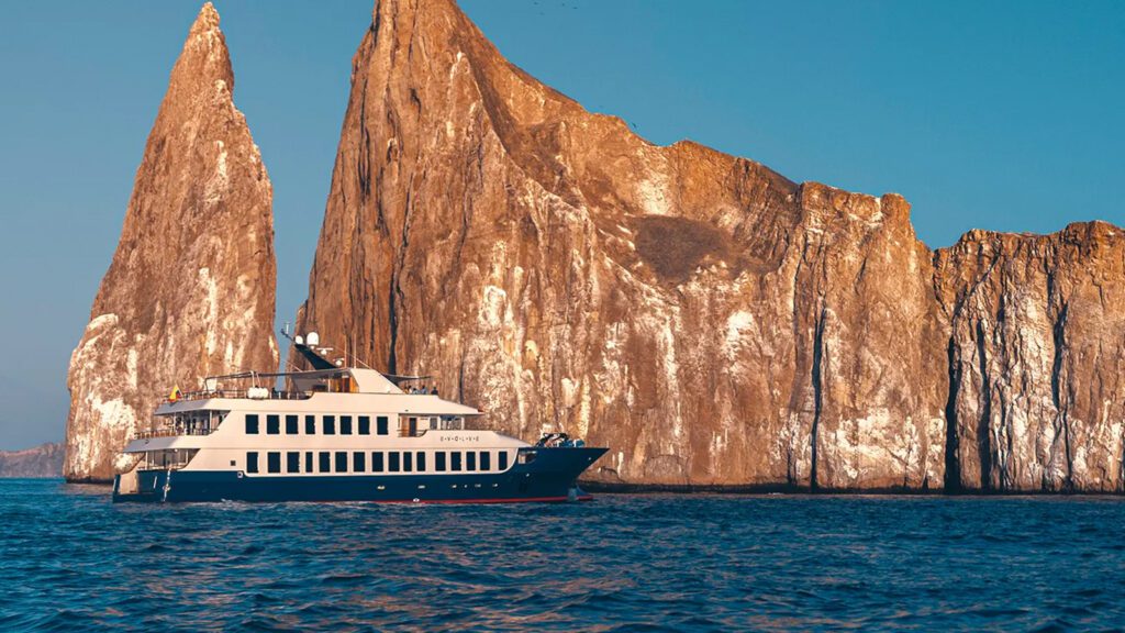 Small expedition yacht anchored in deep blue sea with unique rock formation in the background