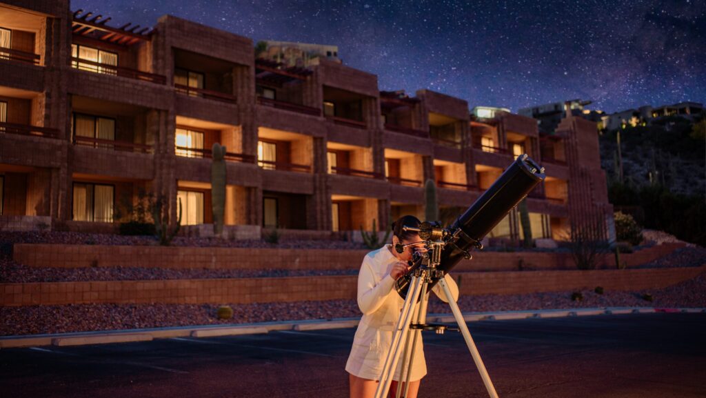 A woman looking through a telescope at night at Loews Ventana Canyon Resort