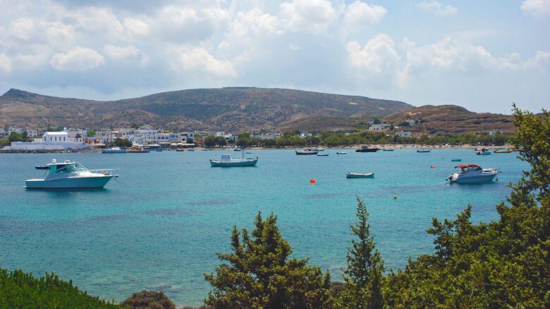 Fishing boats anchored in bay with mountains and small village in background