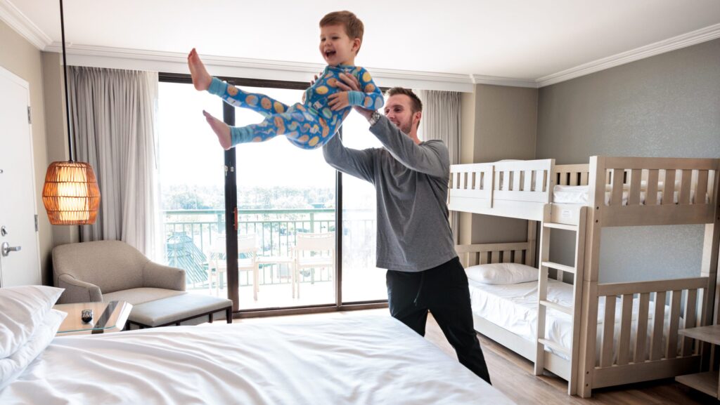A dad playfully tossing a little boy onto the bed in one of the Family Bunk Bed Suites at Orlando World Center Marriott