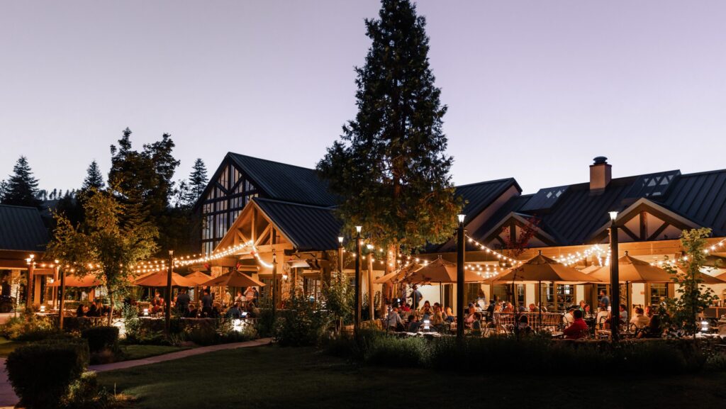 People eating and gathering outside under strings of lights at nighttime at Tenaya at Yosemite