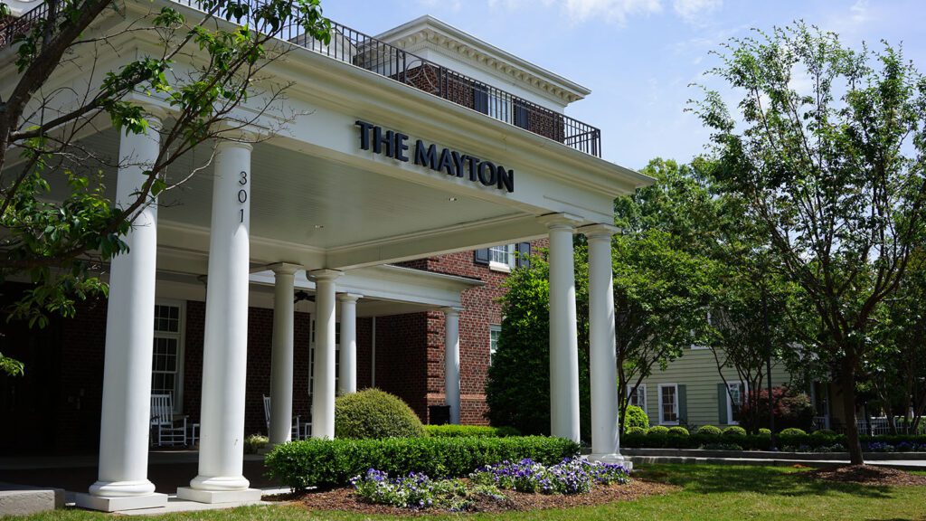 Brick hotel building with white columns at entryway and trees all around
