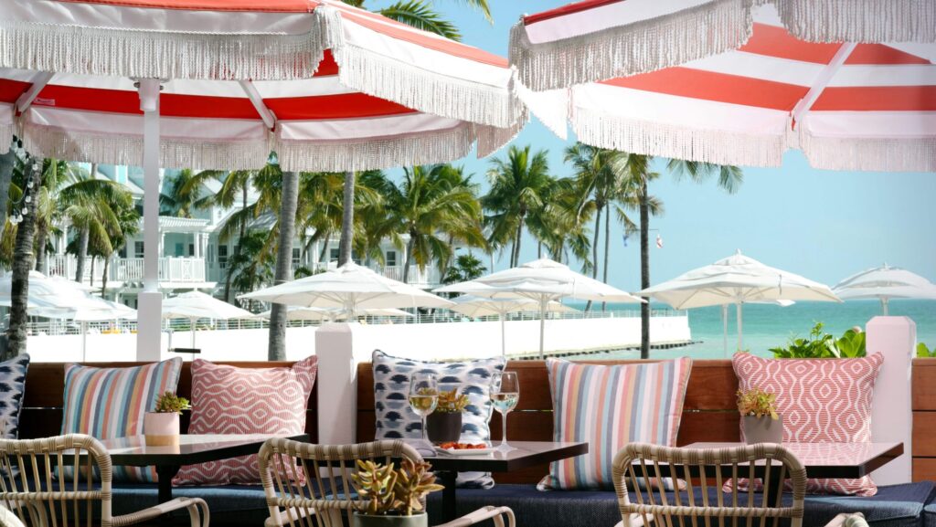 Pink and white striped umbrellas shade tables with pillow-topped benches on the Dewey Deck overlooking the ocean at Southernmost Beach Resort
