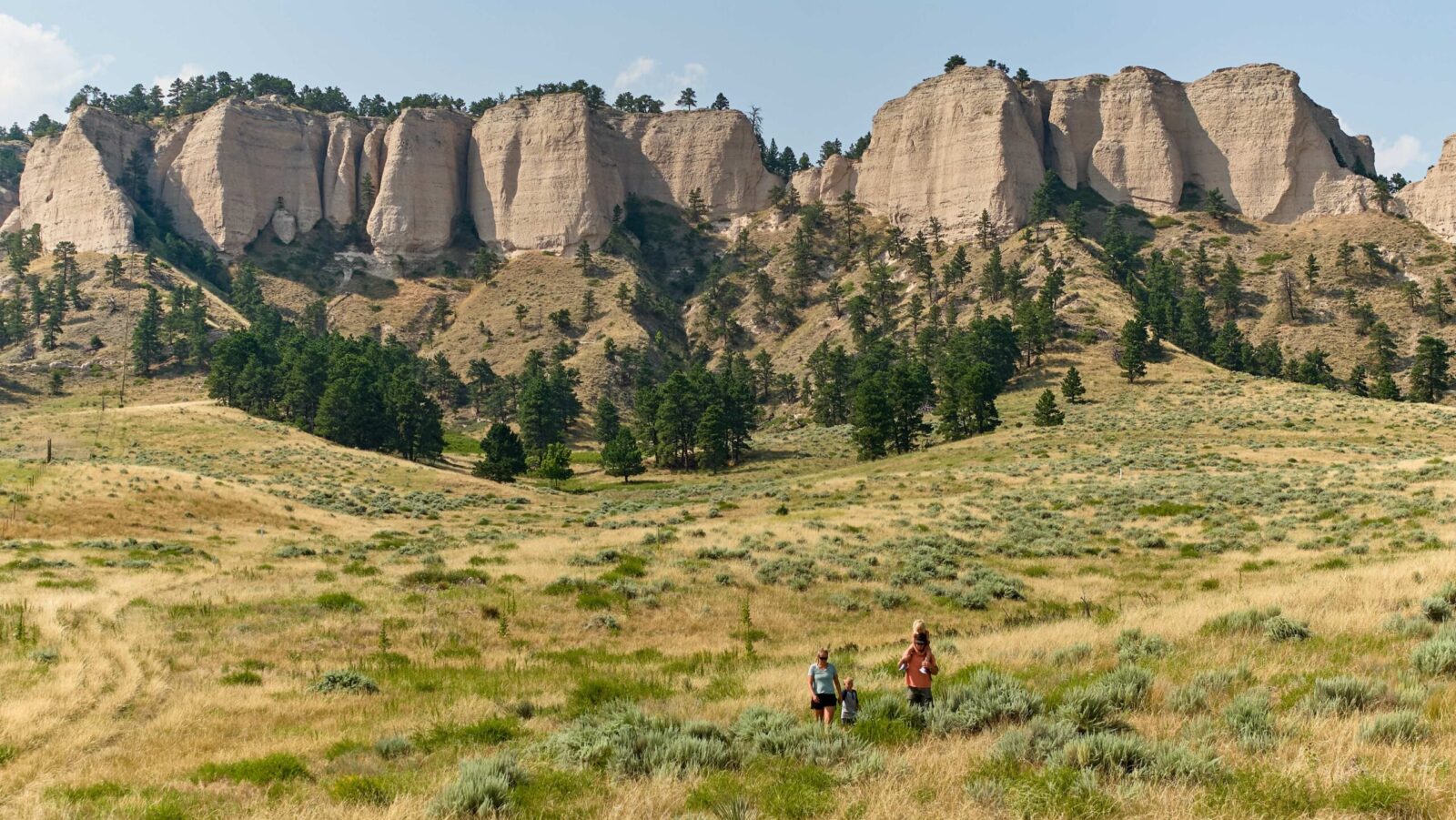 A family hiking through a field with rocky cliffs behind them at Fort Robinson State Park