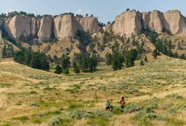 A family hiking through a field with rocky cliffs behind them at Fort Robinson State Park