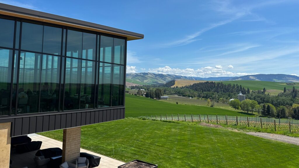 A glass-walled tasting room overlooking green fields and mountains at Echolands Winery