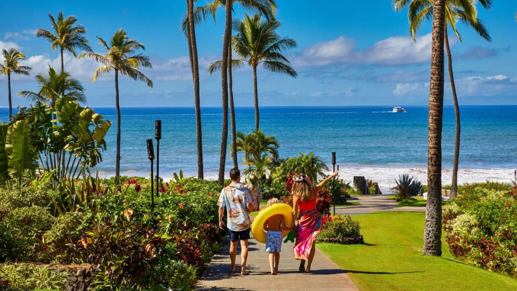 A family with a pool float walking on a path toward the beach at Fairmont Kea Lani