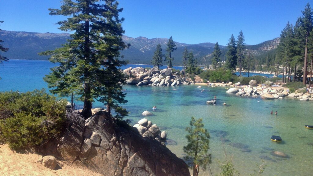 Some swimmers in turquoise colored water with mountains in the distance at Sand Harbor State Park
