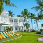 Colorful Adirondack chairs sit on a green lawn with palm trees by the water at Southernmost Beach Resort
