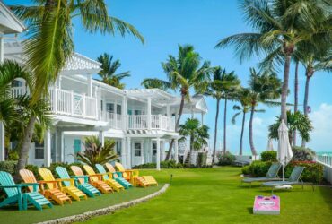 Colorful Adirondack chairs sit on a green lawn with palm trees by the water at Southernmost Beach Resort