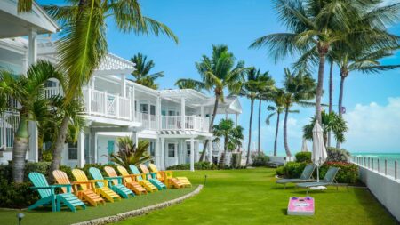Colorful Adirondack chairs sit on a green lawn with palm trees by the water at Southernmost Beach Resort