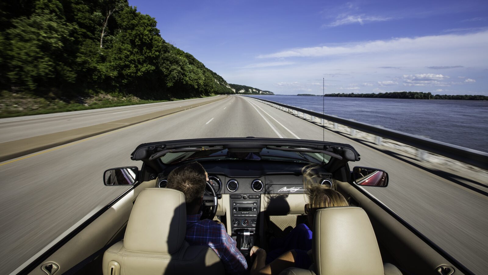 Two people in a convertible driving down Great River Road in Illinois