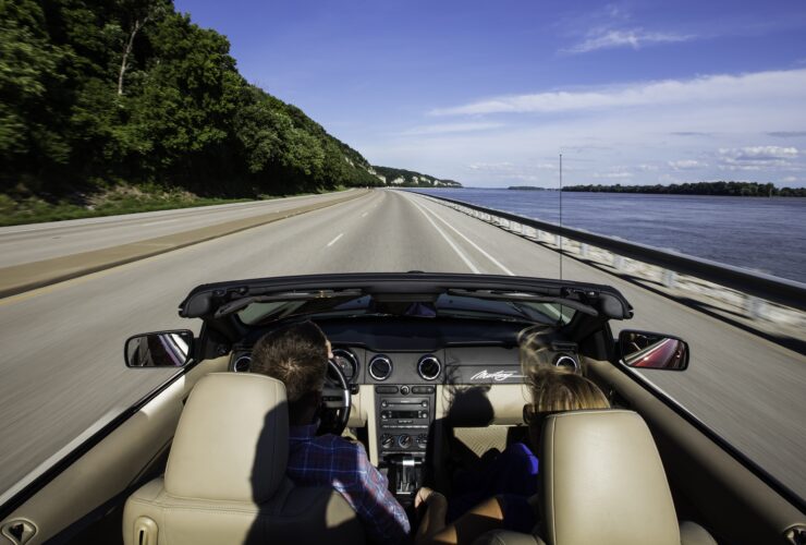 Two people in a convertible driving down Great River Road in Illinois