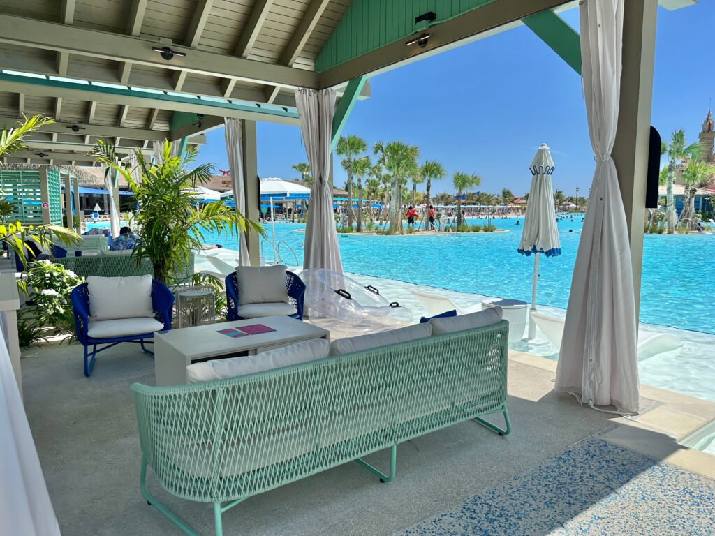 Inside a cabana with a couch, chairs, and table overlooking a pool