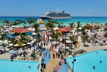 Cruise ship docked at island with many buildings and a pool in the foreground