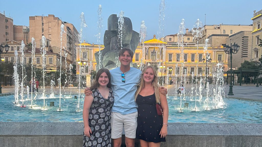 Three teenagers in front of a fountain at twilight in Athens, Greece