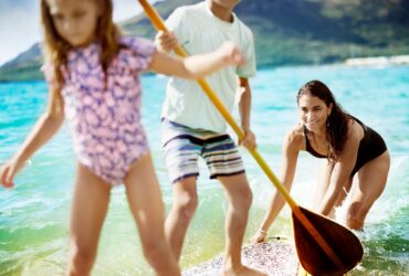 A mom pushing two kids on a paddleboard at The Royal Sonesta Kauaʻi Resort