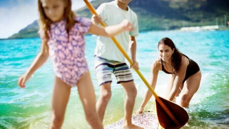 A mom pushing two kids on a paddleboard at The Royal Sonesta Kauaʻi Resort