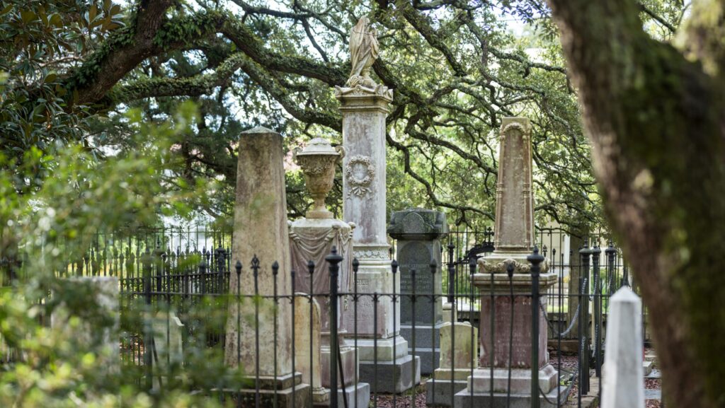 Gravestones surrounded by a fence and trees at the Old Burial Ground in Beaufort, NC