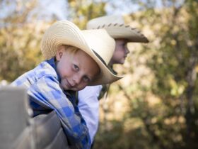 Two kids in cowboy hats leaning on a fence at The Lodge at Blue Sky