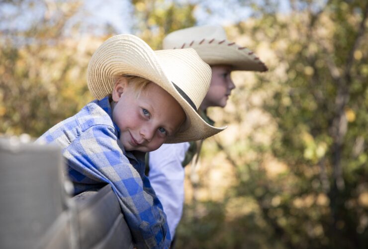Two kids in cowboy hats leaning on a fence at The Lodge at Blue Sky