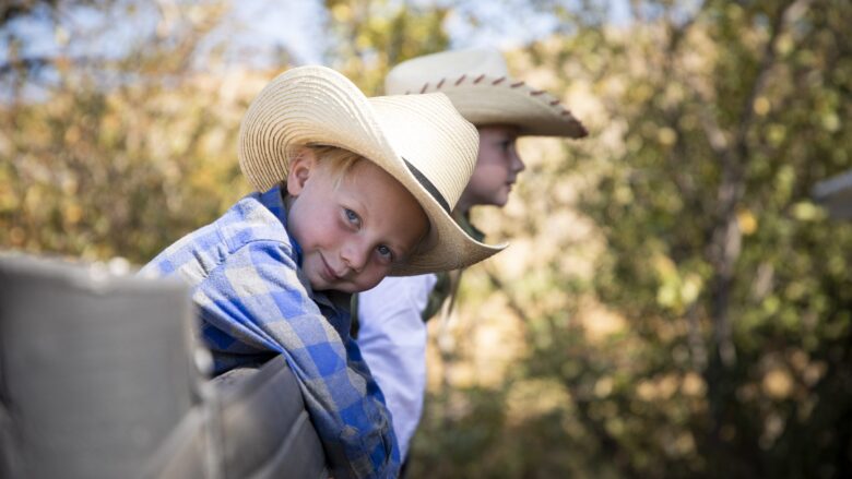 Two kids in cowboy hats leaning on a fence at The Lodge at Blue Sky