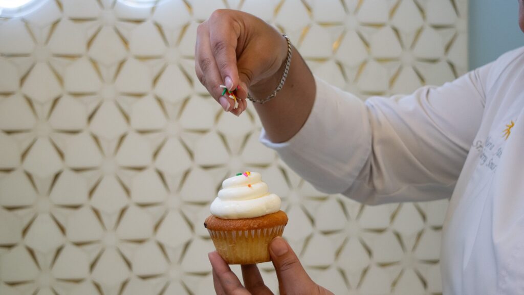 A pastry chef putting sprinkles on a cupcake