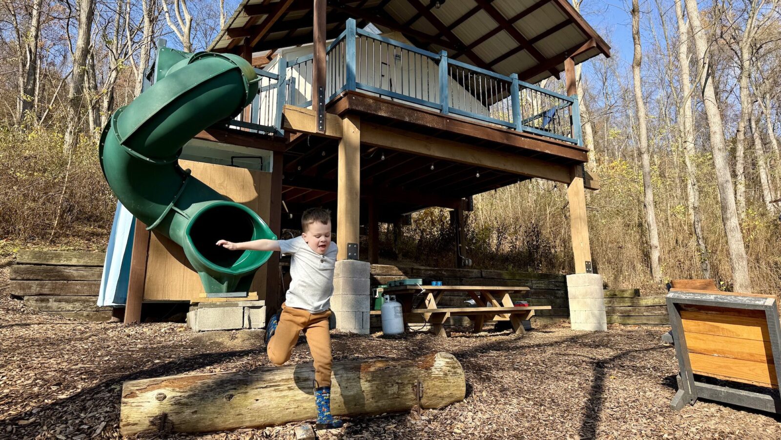 Child jumping over a log with a glamping treehouse accommodation at Airydale retreat in the background