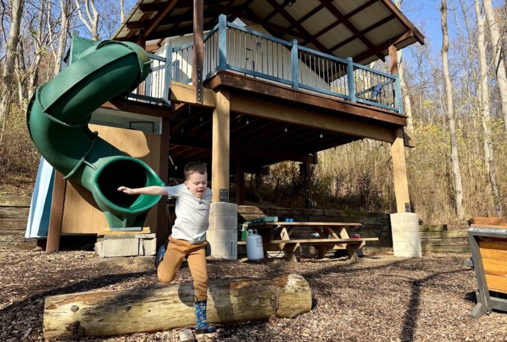 Child jumping over a log with a glamping treehouse accommodation at Airydale retreat in the background