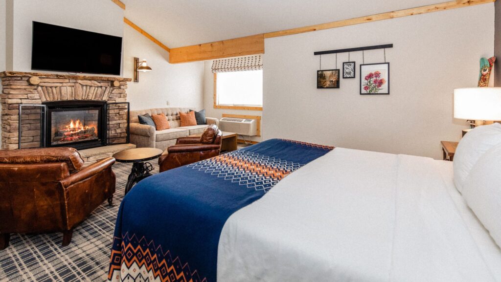 A room with a bed, chairs, and a fire in a stone fireplace at Outbound Mammoth