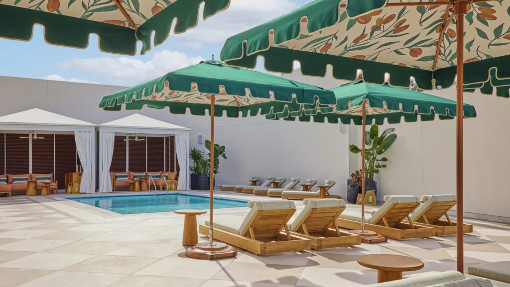A pool surrounded by lounge chairs and green tropical umbrellas at Cameo Beverly Hills