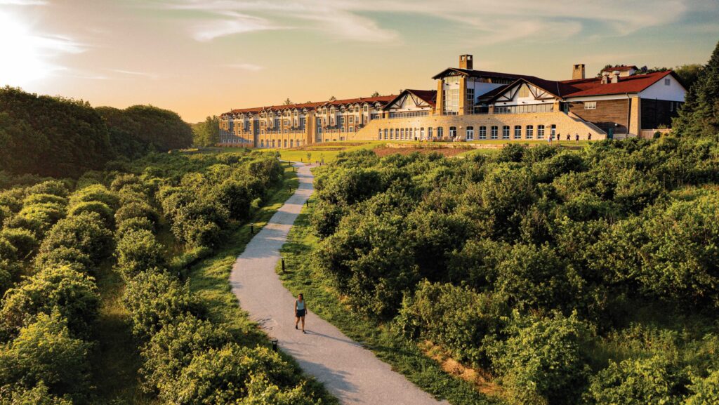A person walking down tree-lined path at Arbor Day Farm with Lied Lodge in the distance